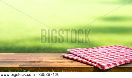 Red Checked Tablecloth On Wood With Blur Green Courtyard Background.summer And Picnic Concepts.desig