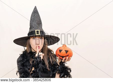 A Beautiful Young Woman In A Halloween Witch Costume Shows A Sign Of Silence With Her Finger And Hol