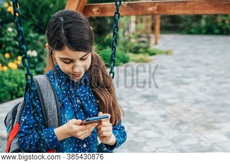 Girl Listening To Music On Her Phone While Sitting On A Swing With A Backpack Behind Her Back