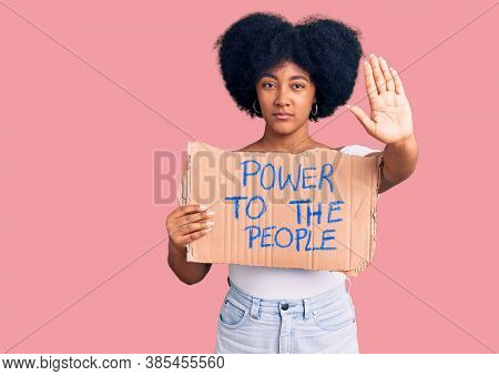 Young african american girl holding power to the people banner with open hand doing stop sign with serious and confident expression, defense gesture 