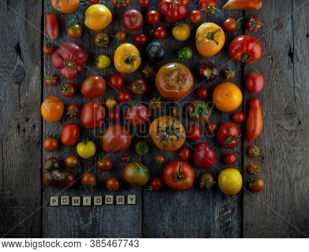 Tomatoes Of Different Varieties And Colors Top View. The Word Tomatoes Is Inscribed In Wooden Letter
