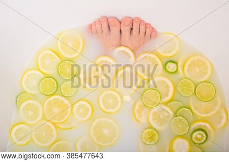Girl Takes A Milk Bath With Lemons And Limes. Citrus Spa. Body Care. Skin Whitening. Womens Feet.