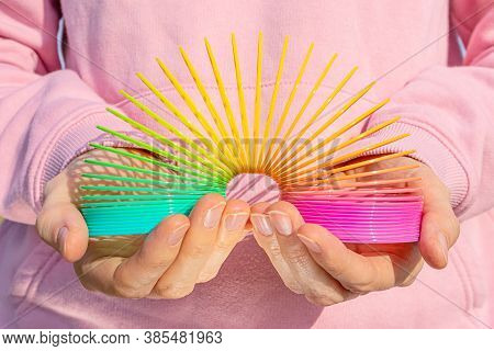 Toy Plastic Rainbow In Hands On The Background Of A Pink Sweatshirt. Colored Spiral For Games And Tr