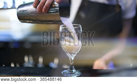 Holding Metal Cup, Pouring Cocktail Into A Glass, Background Of Bartender. Making Cocktail In Night 