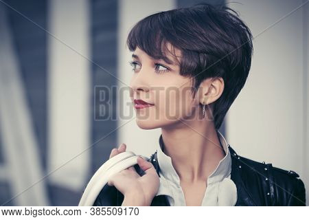 Happy young fashion woman walking on city street Stylish female model in black leather jacket with pixie hair style