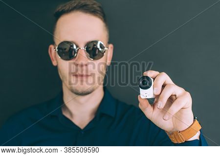 The Guy Takes Photos, Videos With An Action Camera, With One Hand. On A Black Background In The Stud