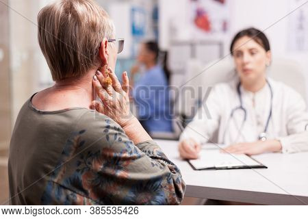 Senior Woman With Neck Pain At Medical Check With Young Doctor In Hospital Cabinet. Doctor Wearing S