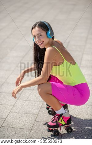 Girl In Bright Sportswear And Roller-skates Sitting On Her Hunkers