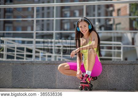 Girl In Bright Sportswear And Roller-skates Sitting On Her Hunkers And Resting