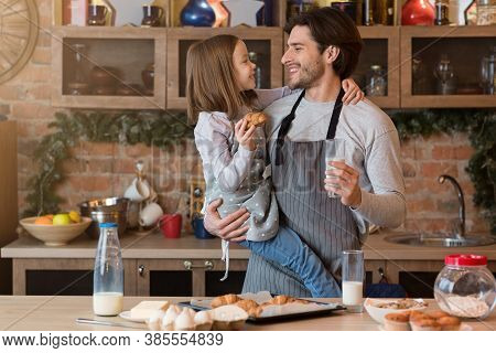 Cheerful Dad And Little Girl Having Snacks In Kitchen, Enjoying Freshly Baked Croissant And Drinking