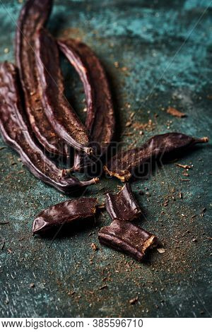 some ripe carob beans on a rustic dark green surface