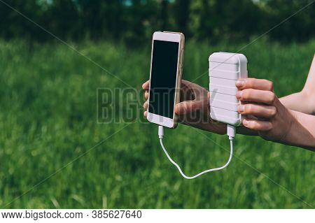 Power Bank And Smartphone In The Girl's Hand. Against The Backdrop Of Nature.