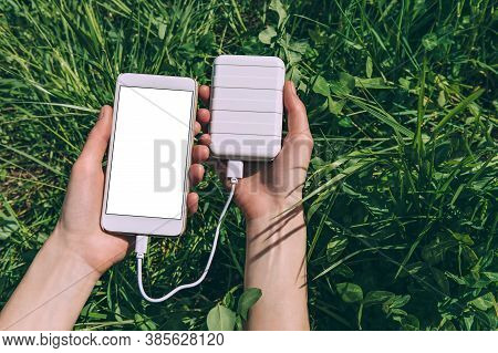 Mock-up Of A Smartphone In The Hands Of A Girl With A Charge From A Power Bank. Against The Backgrou