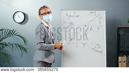Caucasian Young Woman Teacher In Medical Mask At School Writing Formulas And Mahematics Laws On Blac