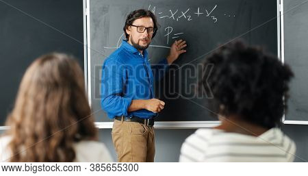 Caucasian Man Teacher At School Writing Formulas And Mathematics Laws On Blackboard. School Concept.