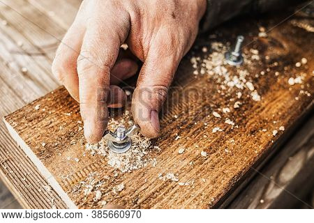 Male Hands Screw A Bolt Into A Wooden Board