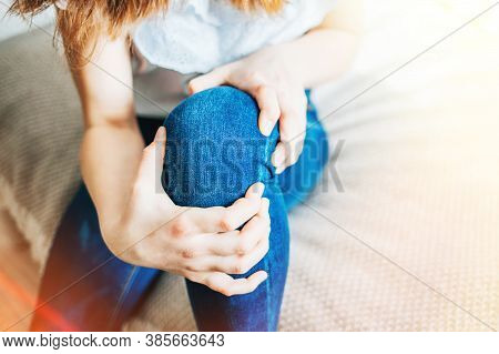 Girl Sitting On Bed Clutching A Sore Knee. Horizontal Shot, Selective Focus, Close-up, Sun Flare