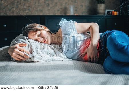 Young Woman Suffering From Abdominal Pain Lying On A Bed At Home