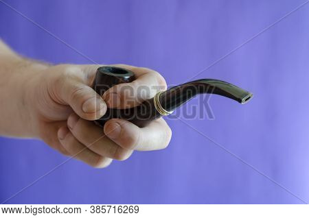 Smoking Pipe In Hand Against The Background Of A Blue Wall. An Adult Male's Right Hand Holds A Smoki