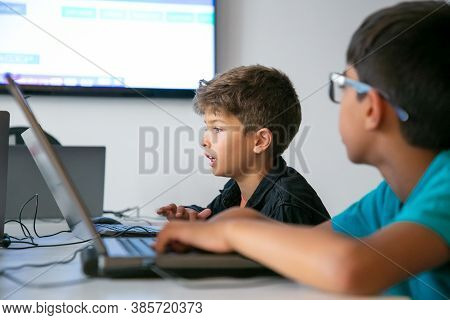Caucasian Boy Reading Task Aloud During Lesson. Classmates And Pupils Sitting At Table In School And