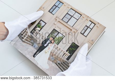 Hands In White Gloves Holding A Photo Book With Wedding Photos. Beautiful And Convenient Storage Of 