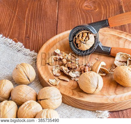 Close-up Of A Walnut And Nutcracker. Freshly Cracked Walnut In A Nutcracker On A Wooden Tray And Bur