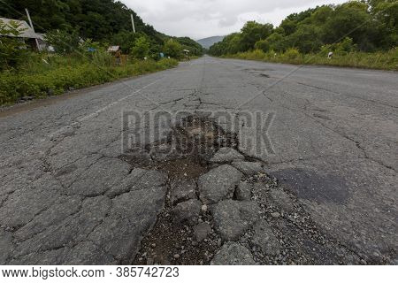 Very Bad Road In Russia. The Asphalt Road Is All In Holes In The Middle Of The Forest.