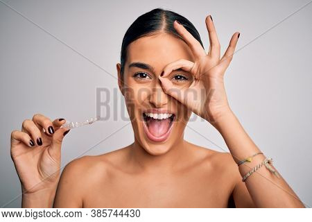 Young beautiful brunette woman holding dental aligner orthodontic to teeth corretion with happy face smiling doing ok sign with hand on eye looking through fingers