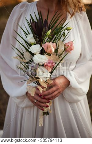 A Bride In A White Wedding Dress Holds A Delicate Bridal Bouquet Of Roses And A Lot Of Greenery. Sty