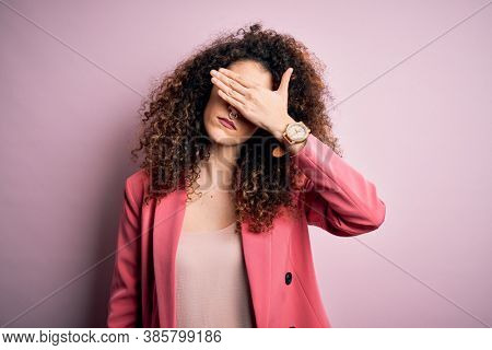 Young beautiful businesswoman with curly hair and piercing wearing elegant jacket covering eyes with hand, looking serious and sad. Sightless, hiding and rejection concept