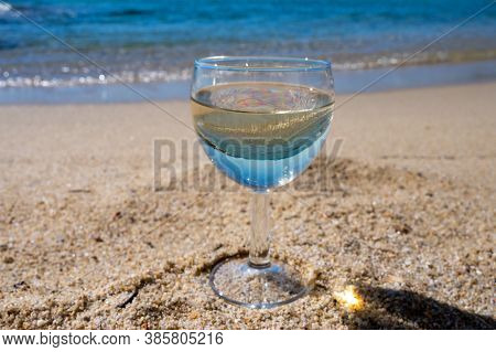 Glass Of Local Dry White Wine On White Sandy Beach And Blue Mediterranean Sea On Background, Near Le