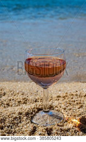 Glass Of Local Rose Wine On White Sandy Beach And Blue Mediterranean Sea On Background, Near Le Lava