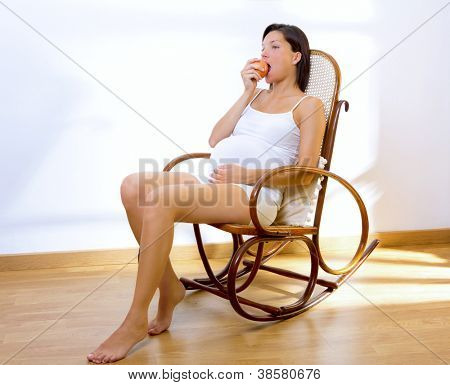 Bella donna incinta mangia una mela a casa seduto sulla sedia rocker