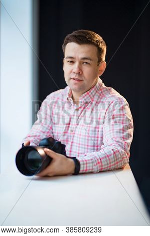 A Male Photographer In A Checkered Shirt Sits At A Table And Holds A Camera In His Hands. Creative P