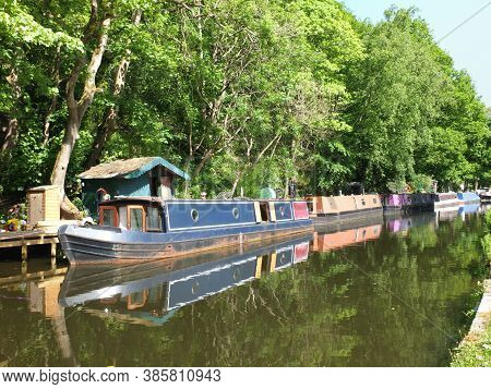 Old Canal Boats Moored On The Rochdale Canal Near Hebden Bridge Surrounded By Trees In Summer Sunlig