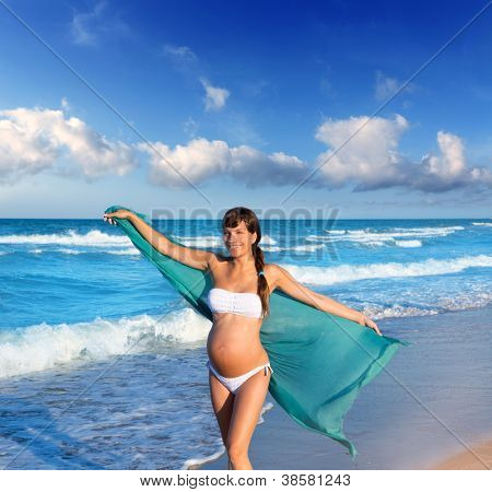 Bella donna incinta camminando sulla spiaggia blu in estate con il fazzoletto di vento di salto