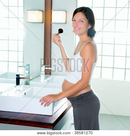 Bella donna incinta sul trucco di bagno moderno con pennello nello specchio