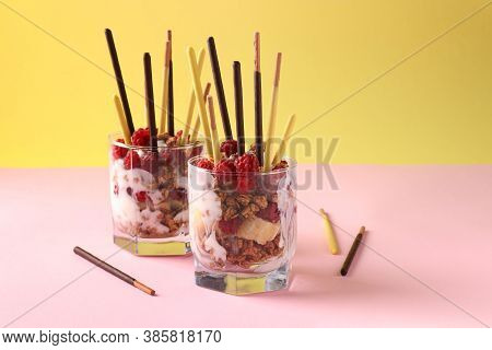 Dessert In Two Glasses With Chocolate Granola, Banana And Raspberry, Decorated With Sticks Pocky On 