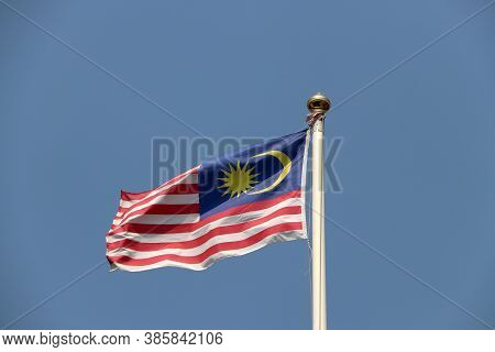National Flag Of Malaysia On Bright Blue Sky Background. Blown Away By Wind. Malaysia Is One Of The 