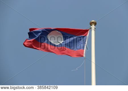 National Flag Of Laos On Bright Blue Sky Background. Blown Away By Wind. Laos Is One Of The Ten Asso