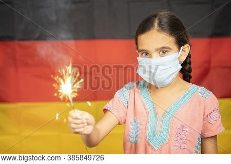 Young Girl Kid On Medical Mask Holding Sparkler With German Flag As Background - Concept Showing Cel