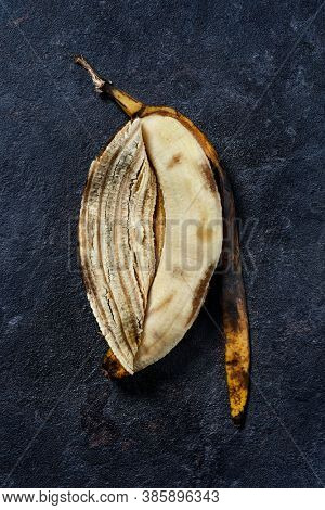 high angle view of a peeled overripe banana and its skin on a black stone surface