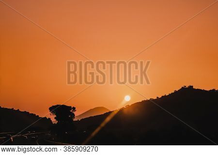 Beautiful Orange Sky Sunset On Highway With Cars Driving Around The Mountains With Sun Above And Ced