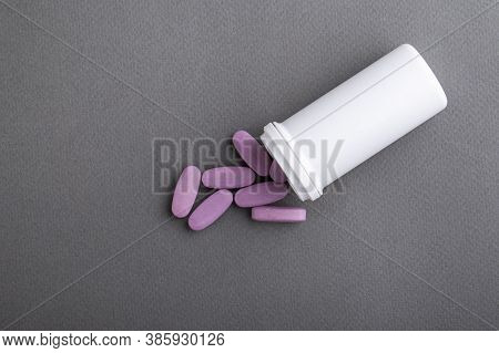 Lilac Medical Pills Are Falling Out Of A White Bottle On A Gray Background. Concept Of Health, Drug 