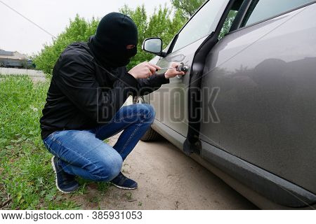 Breaking Into The Car. Theft Auto. The Malefactor In A Black Mask Opens A Door In A Car.