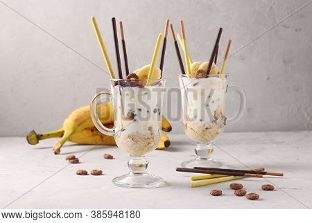 Two Glasses Of Granola With Chocolate And Banana, Decorated With Sticks Pocky On Gray Background