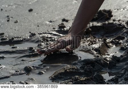 Sihouette Of A Child's Hand Playing In The Mud Or Sand At The Beack On A Sunny Day.