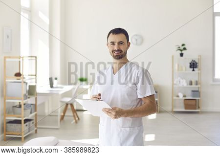 Smiling Man Doctor Chiropractor Or Osteopath Standing With Notes And Looking At Camera
