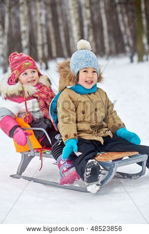 Twee kleine kinderen glimlachen zitten in slee in winter park