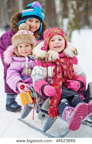 Meisje duwt slee met twee jongere kinderen in winter park